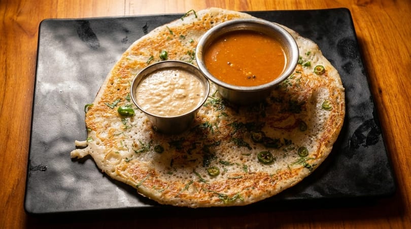 A savory dosa pancake with green chilies and herbs, served with two dipping sauces.