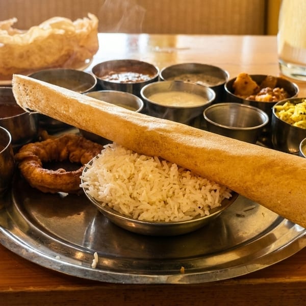 A South Indian thali meal with dosa, rice, curries, and fried snacks on a wooden table.